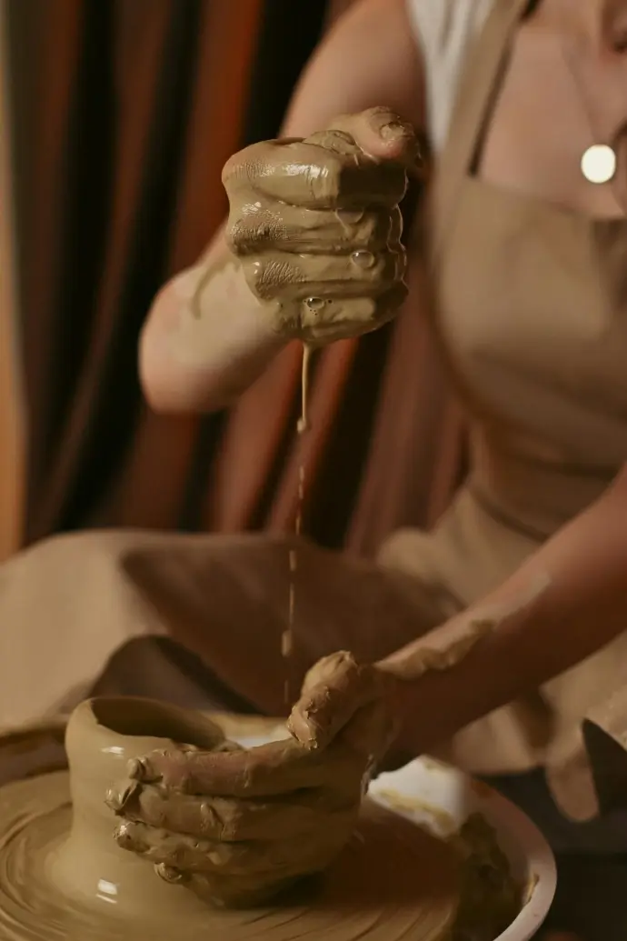 Potter applying water to their hands as they throw a fclay orm on their pottery wheel