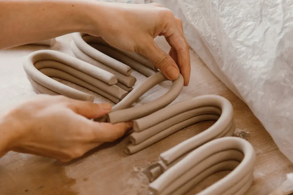 Hands laying coils of clay in arches for handbuilding clay forms
