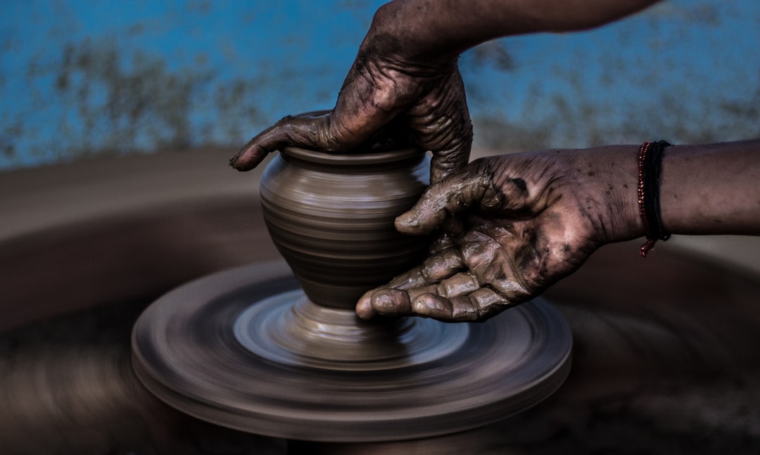 Hands forming a vase out of dark clay on a spinning pottery wheel