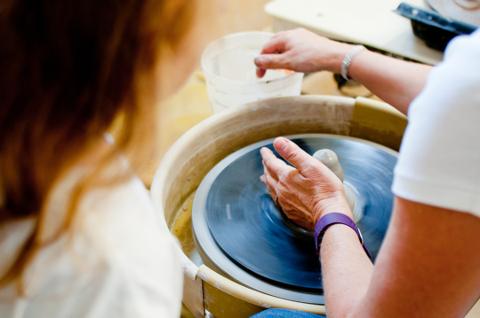 Teacher leaning over a student working on a pottery wheel